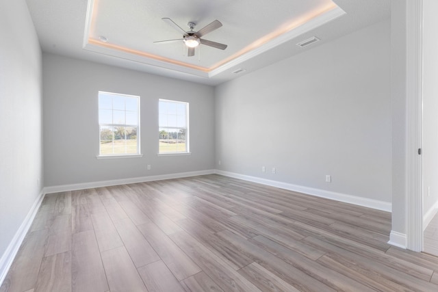 unfurnished room with visible vents, baseboards, a raised ceiling, a ceiling fan, and wood finished floors