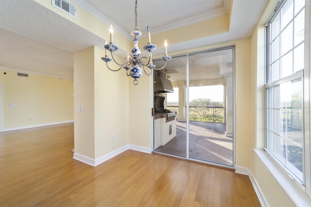 unfurnished dining area with a raised ceiling, crown molding, a textured ceiling, wood-type flooring, and a chandelier