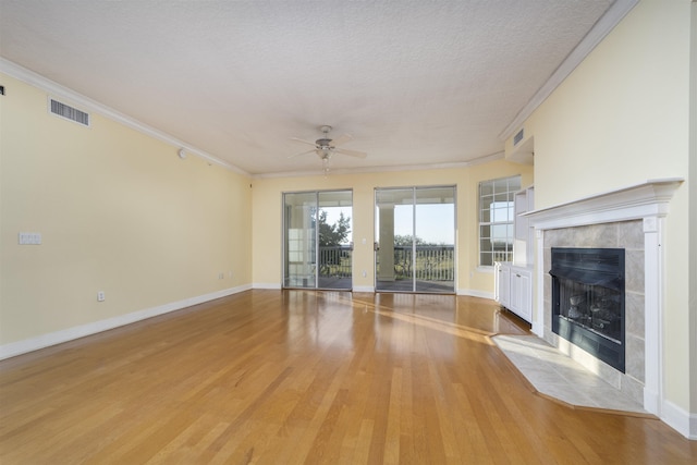 unfurnished living room featuring light wood-type flooring, ornamental molding, a textured ceiling, ceiling fan, and a fireplace