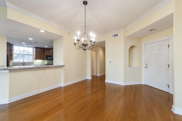 unfurnished dining area featuring a textured ceiling, an inviting chandelier, dark hardwood / wood-style floors, and ornamental molding