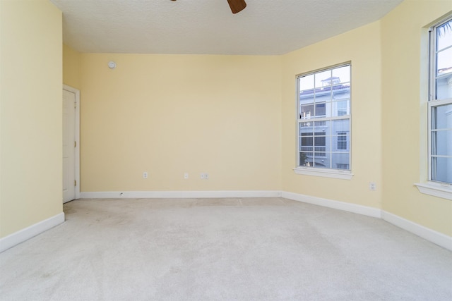 empty room with light carpet, plenty of natural light, ceiling fan, and a textured ceiling