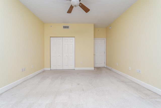 unfurnished bedroom featuring ceiling fan, a closet, light carpet, and a textured ceiling