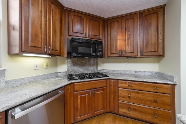 kitchen featuring light stone counters, black appliances, a textured ceiling, and light wood-type flooring