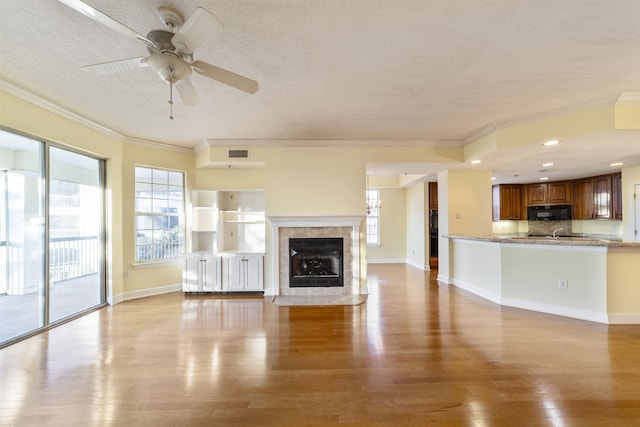 unfurnished living room featuring ceiling fan, crown molding, light wood-type flooring, and a textured ceiling