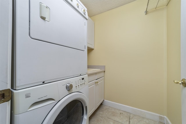 clothes washing area featuring a textured ceiling, cabinets, light tile patterned floors, and stacked washer / dryer