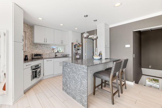 kitchen with a kitchen bar, a peninsula, white cabinets, stainless steel appliances, and a sink