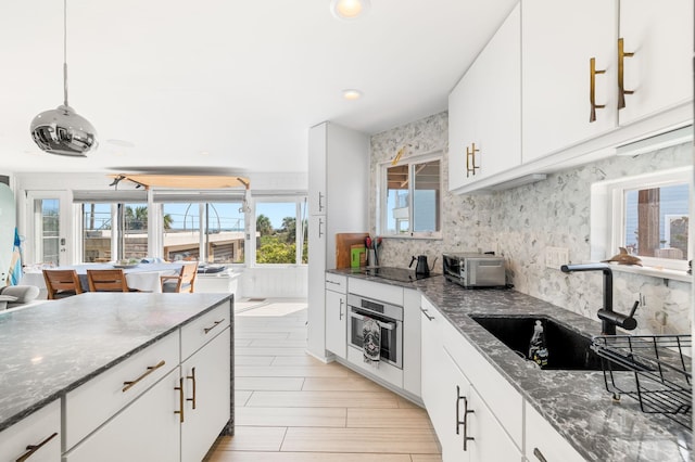 kitchen with oven, a sink, white cabinets, decorative backsplash, and black electric stovetop