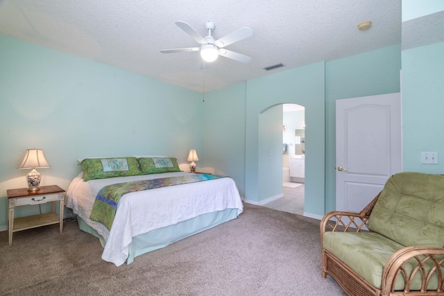 carpeted bedroom with visible vents, arched walkways, a ceiling fan, ensuite bathroom, and a textured ceiling