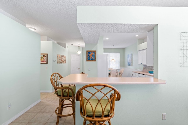 kitchen with light tile patterned floors, white cabinets, a breakfast bar area, a peninsula, and light countertops