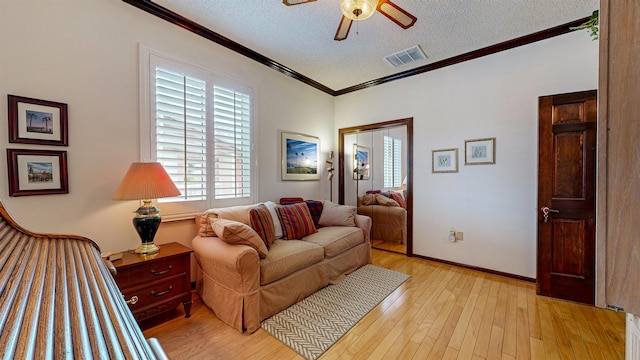 living area featuring crown molding, light wood-style flooring, a textured ceiling, a ceiling fan, and visible vents