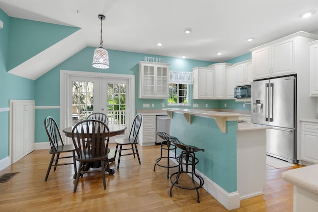 kitchen with hanging light fixtures, stainless steel appliances, vaulted ceiling, white cabinets, and light wood-type flooring