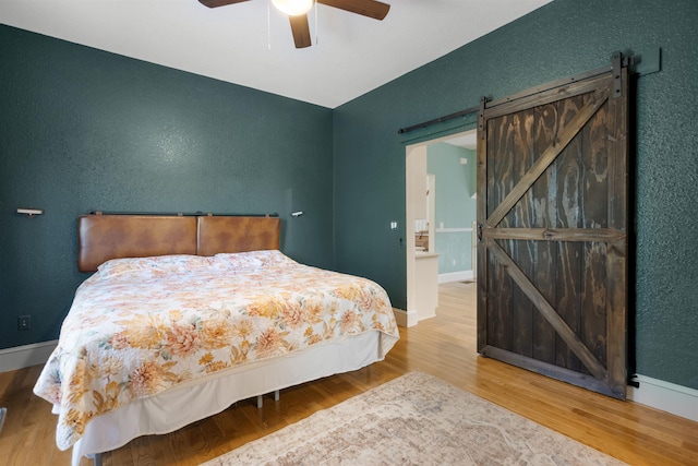 bedroom featuring hardwood / wood-style flooring, ceiling fan, and a barn door