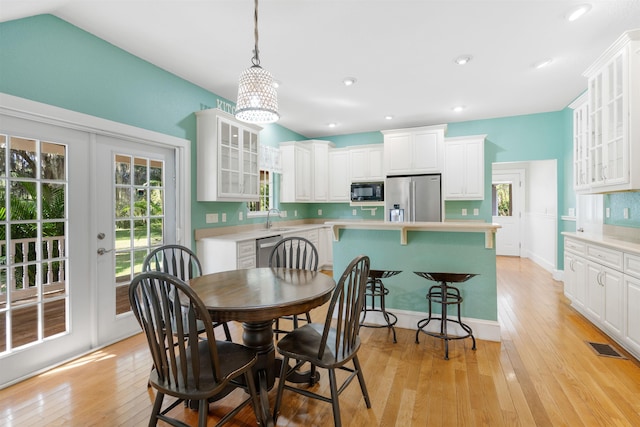 dining space featuring french doors, sink, vaulted ceiling, light wood-type flooring, and a notable chandelier