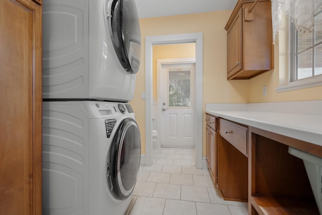 laundry area featuring cabinets, light tile patterned floors, and stacked washer and clothes dryer