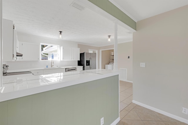 kitchen with sink, light tile patterned floors, appliances with stainless steel finishes, white cabinets, and kitchen peninsula