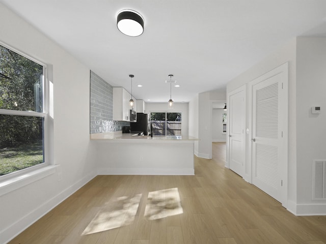 kitchen featuring decorative light fixtures, light wood-type flooring, kitchen peninsula, white cabinets, and backsplash