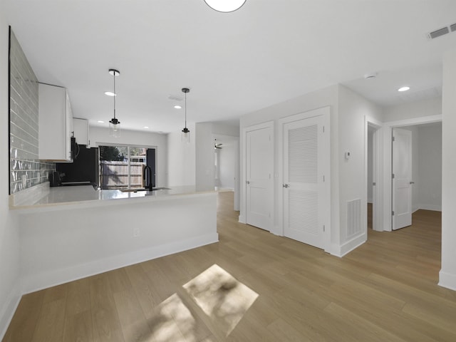 kitchen with pendant lighting, white cabinetry, black refrigerator, light hardwood / wood-style floors, and kitchen peninsula