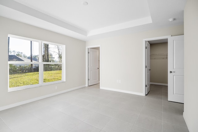 unfurnished bedroom with light tile patterned floors, a walk in closet, a closet, and a raised ceiling