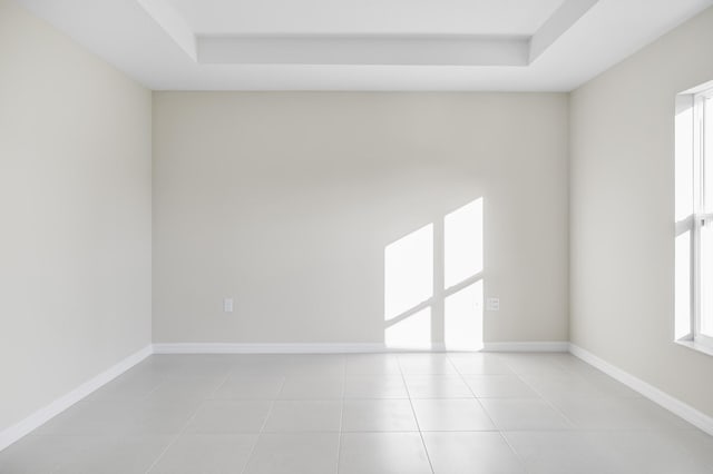 tiled empty room featuring a raised ceiling