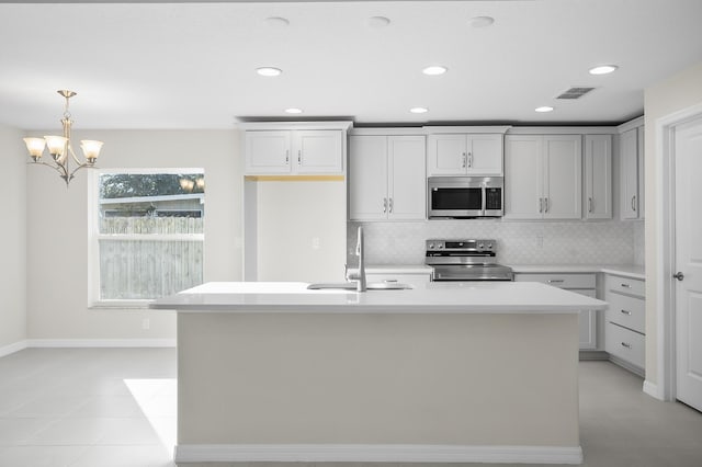 kitchen featuring sink, decorative light fixtures, stainless steel appliances, a kitchen island with sink, and backsplash