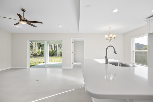 kitchen with pendant lighting, sink, light tile patterned floors, white cabinets, and a center island with sink