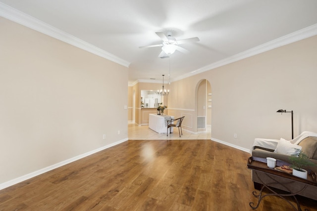 living room featuring baseboards, arched walkways, wood finished floors, crown molding, and ceiling fan with notable chandelier