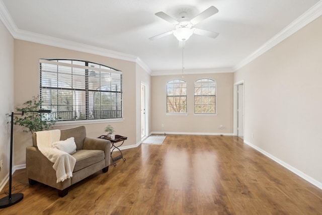 living area with ornamental molding, wood finished floors, a ceiling fan, and baseboards