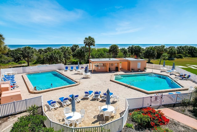 community pool with a patio, fence, and a water view