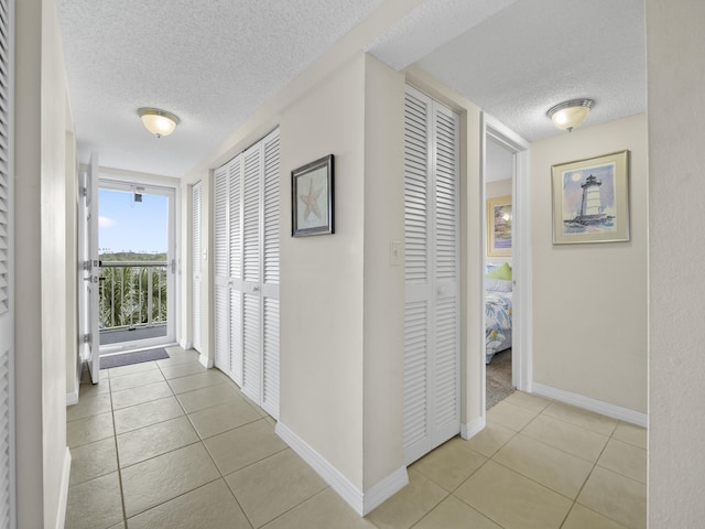 hall with light tile patterned floors, baseboards, and a textured ceiling