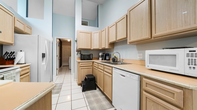 kitchen with light tile patterned floors, white appliances, sink, and light brown cabinetry