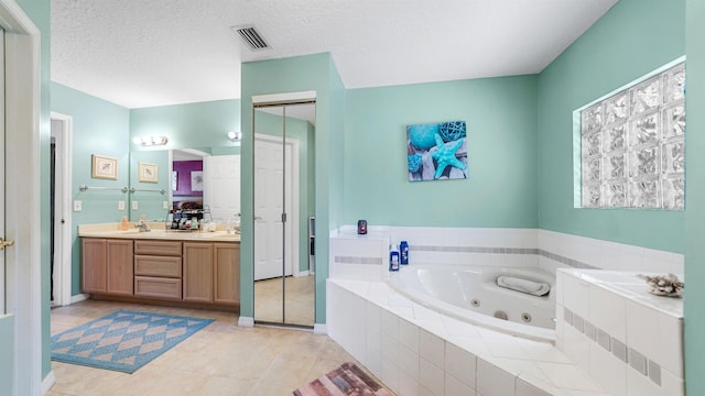 bathroom featuring tile patterned flooring, a relaxing tiled tub, a textured ceiling, and vanity