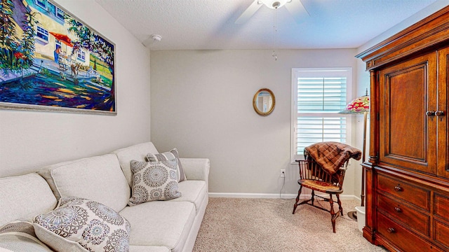 living area featuring ceiling fan, light colored carpet, and a textured ceiling