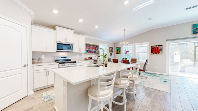 kitchen with appliances with stainless steel finishes, lofted ceiling, sink, white cabinets, and a kitchen island with sink