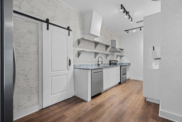 kitchen featuring white cabinets, a sink, a barn door, rail lighting, and appliances with stainless steel finishes