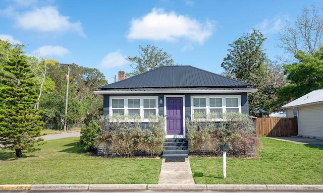bungalow-style home featuring metal roof, a chimney, a front yard, and fence