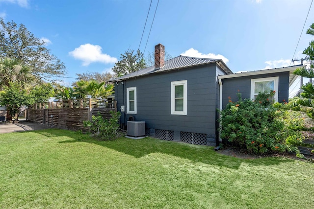 back of property featuring a chimney, central AC unit, fence, a yard, and metal roof