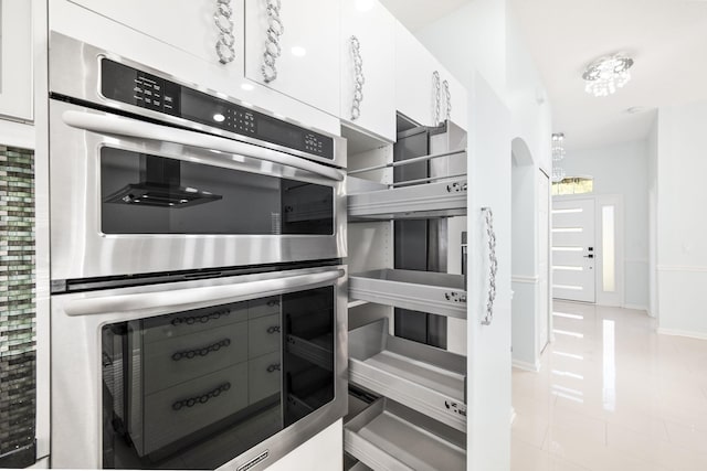 kitchen featuring white cabinets, stainless steel double oven, a chandelier, and light tile patterned flooring