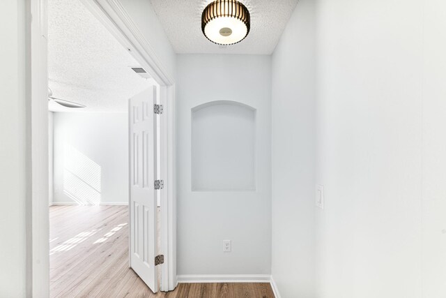 hall with a textured ceiling and light hardwood / wood-style floors