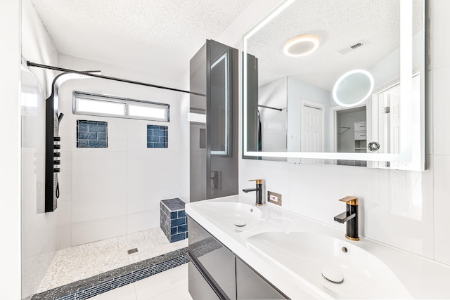 bathroom featuring a tile shower, tile patterned floors, vanity, and a textured ceiling