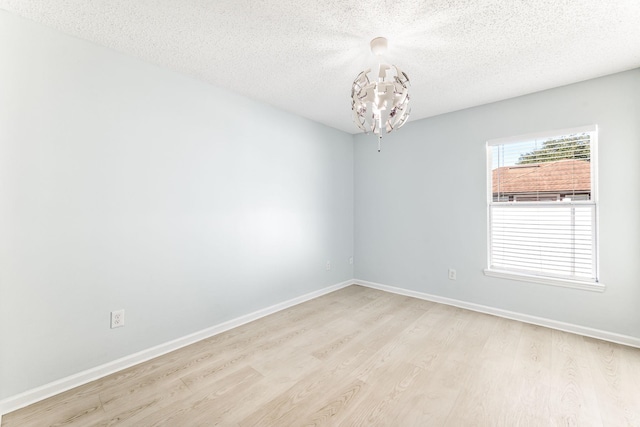 spare room featuring a notable chandelier, light wood-type flooring, and a textured ceiling