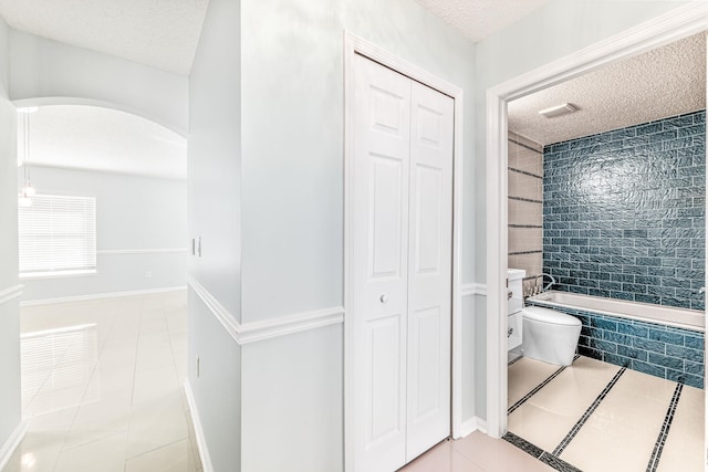 bathroom featuring tile patterned flooring, a textured ceiling, toilet, tile walls, and tiled shower / bath