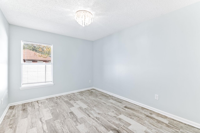 unfurnished room featuring a notable chandelier, light hardwood / wood-style floors, and a textured ceiling