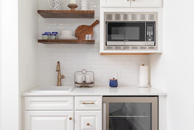 bar with wine cooler, sink, stainless steel microwave, decorative backsplash, and white cabinets