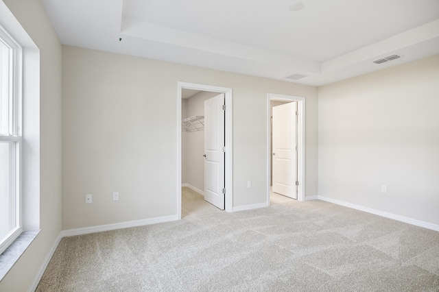 unfurnished bedroom featuring a tray ceiling, a walk in closet, and light colored carpet