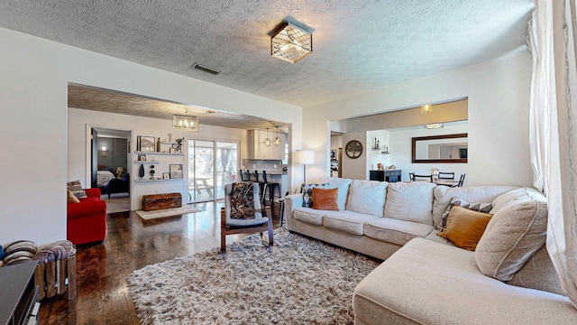 living area with a notable chandelier, a textured ceiling, visible vents, and dark wood-type flooring