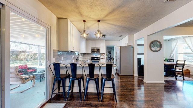 kitchen featuring tasteful backsplash, dark wood-style flooring, a peninsula, hanging light fixtures, and stainless steel appliances