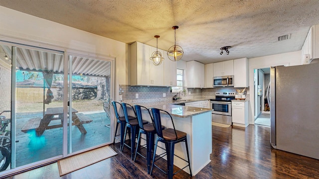 kitchen featuring dark wood-style flooring, backsplash, appliances with stainless steel finishes, white cabinets, and a peninsula