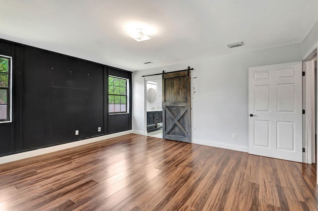 132 Southwind Cir, Saint Augustine, FL 32080 - unfurnished bedroom with a barn door, wood finished floors, and connected bathroom