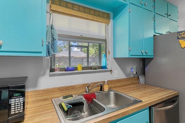 kitchen featuring a sink, dishwasher, blue cabinetry, and freestanding refrigerator