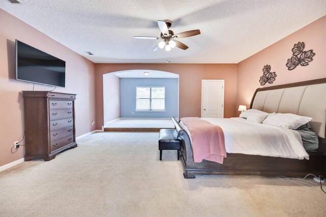 bedroom featuring a textured ceiling, light colored carpet, and ceiling fan